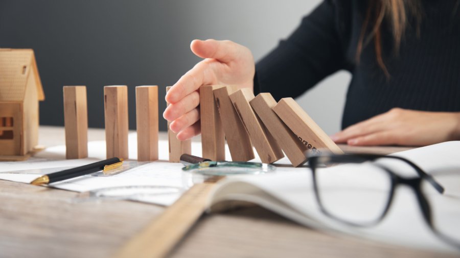 woman hand stops wooden dominoes from falling on wooden house model